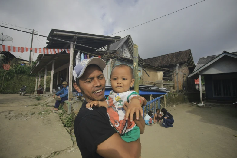 a man holds his baby in front of some houses