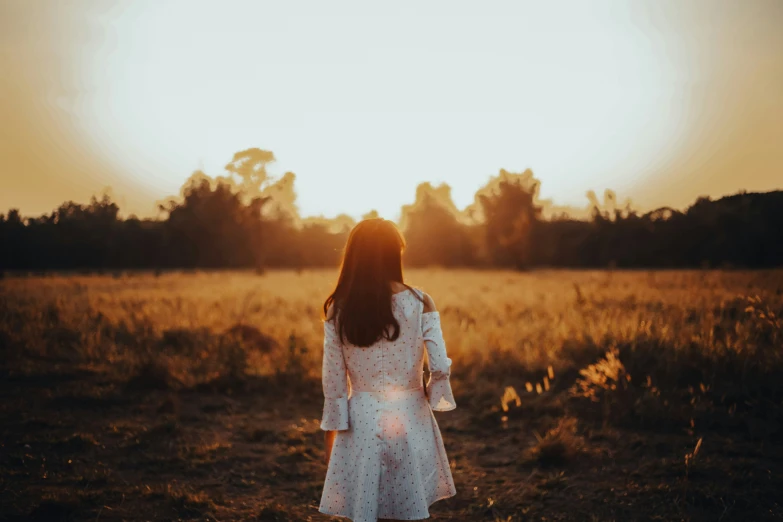 a woman stands alone in a field as the sun goes down