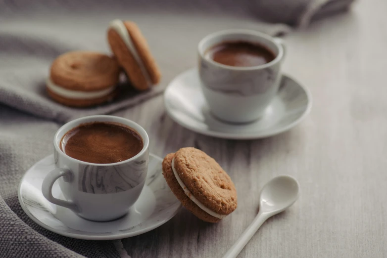 two cups of coffee next to a spoon and cookies