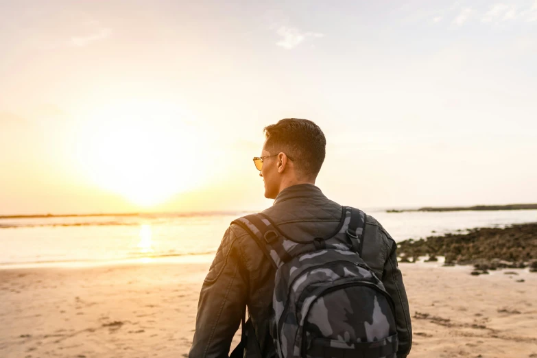 a man walking along the beach, with a back pack in his hand