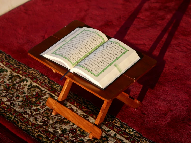 the holy book is sitting on a wooden stand with red rug in background
