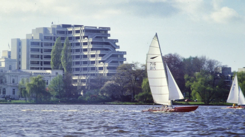 three sail boats sailing through the water with a city in the background