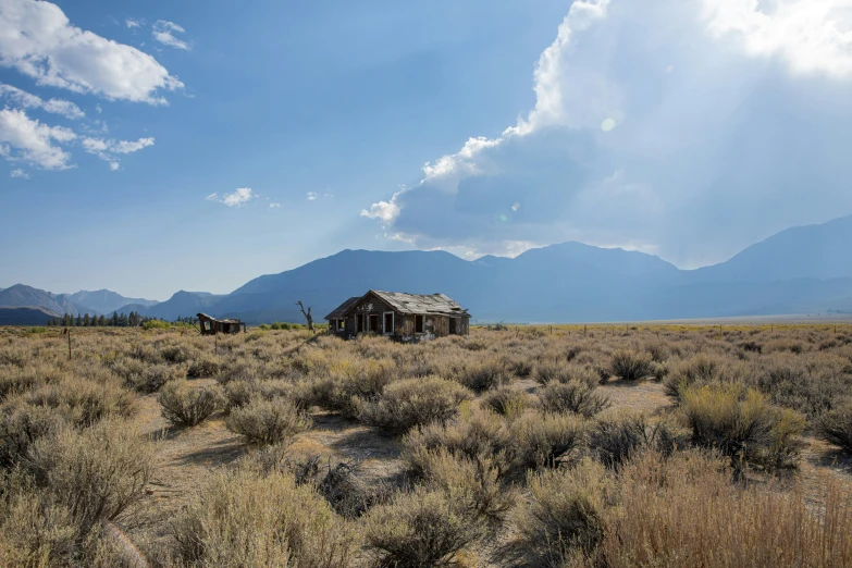 an old abandoned home in a field near the mountains