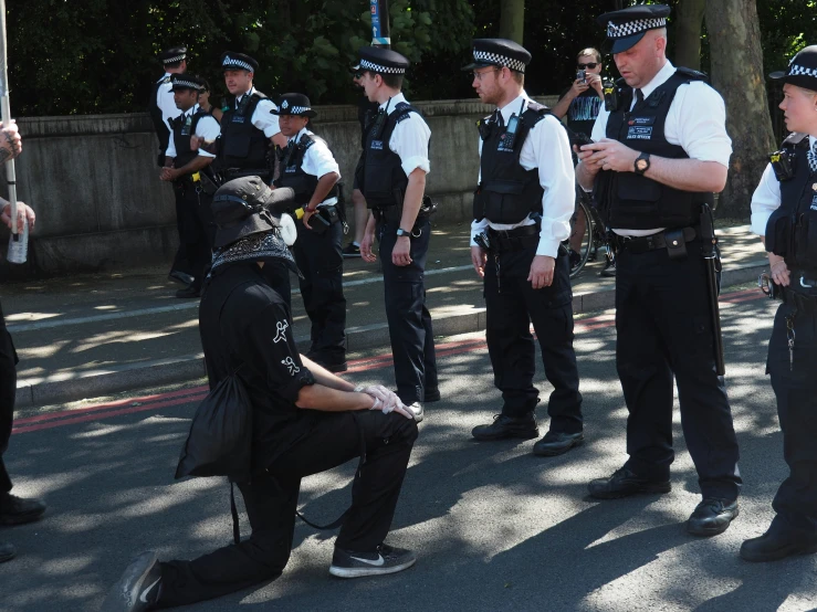 a man kneels down on the ground as a group of police men look on