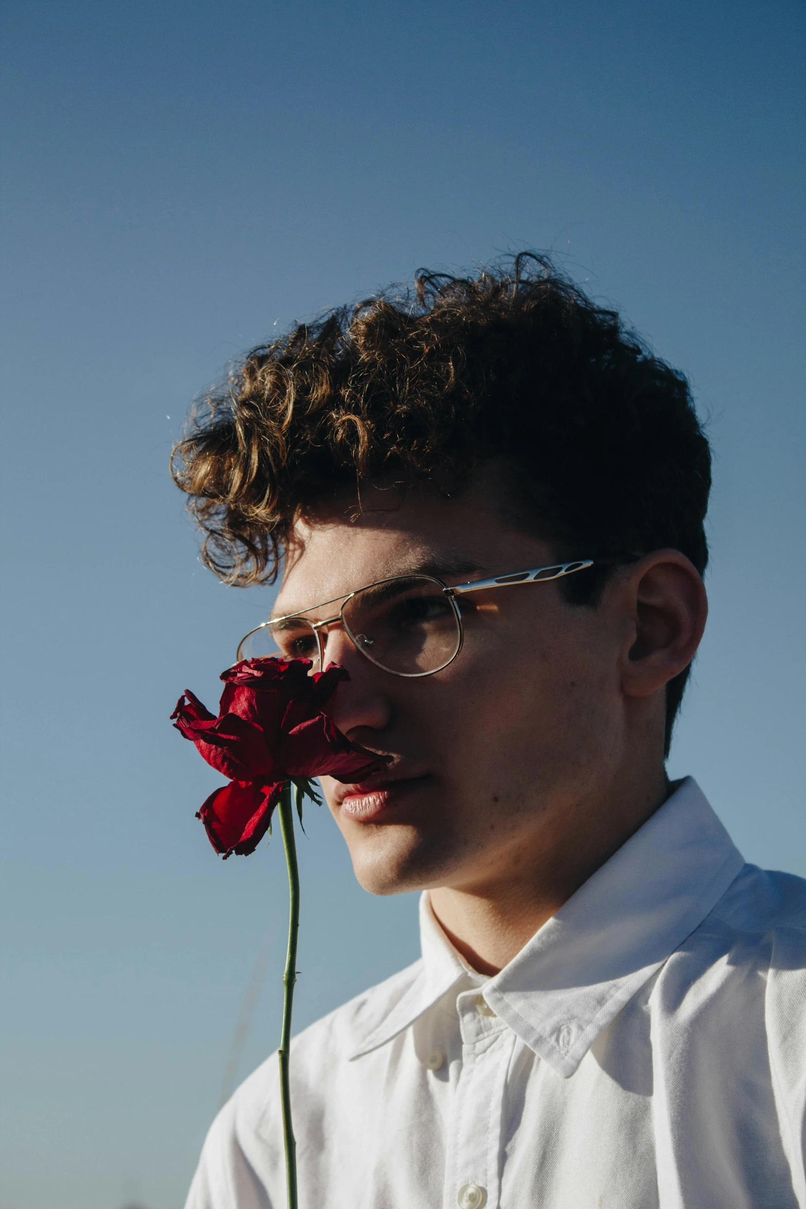 a man holding a red flower behind his face