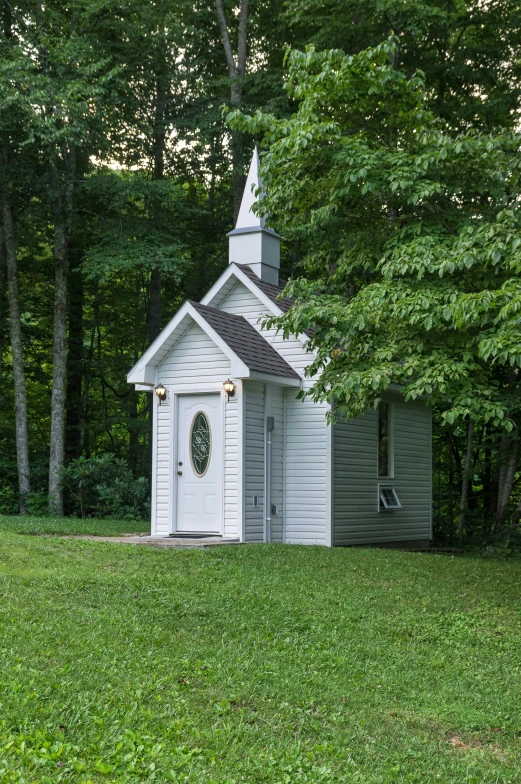 a small white church on a green lawn surrounded by trees