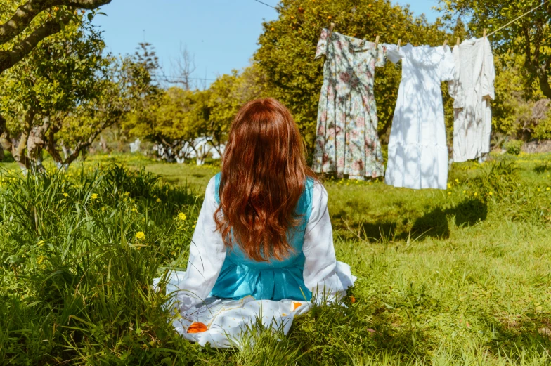 a woman sits and looks at clothes hanging on a line