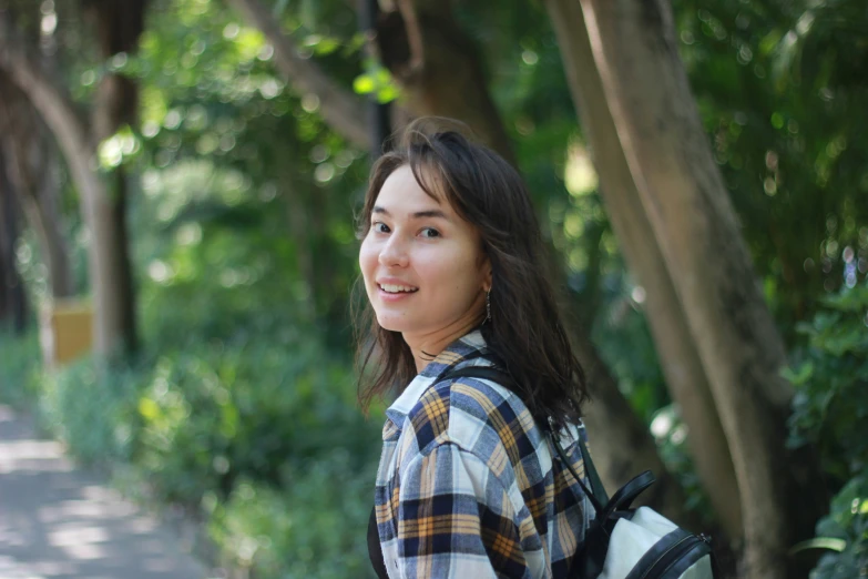 the young woman smiles as she walks by some trees