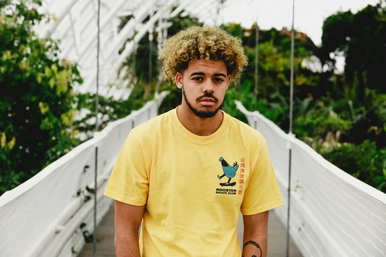 a young man posing on a bridge in a yellow shirt