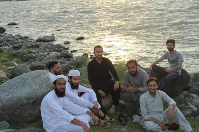 men are sitting on the shore near some rocks