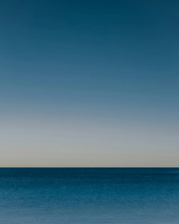 a lone man surfing in the ocean under an almost empty blue sky