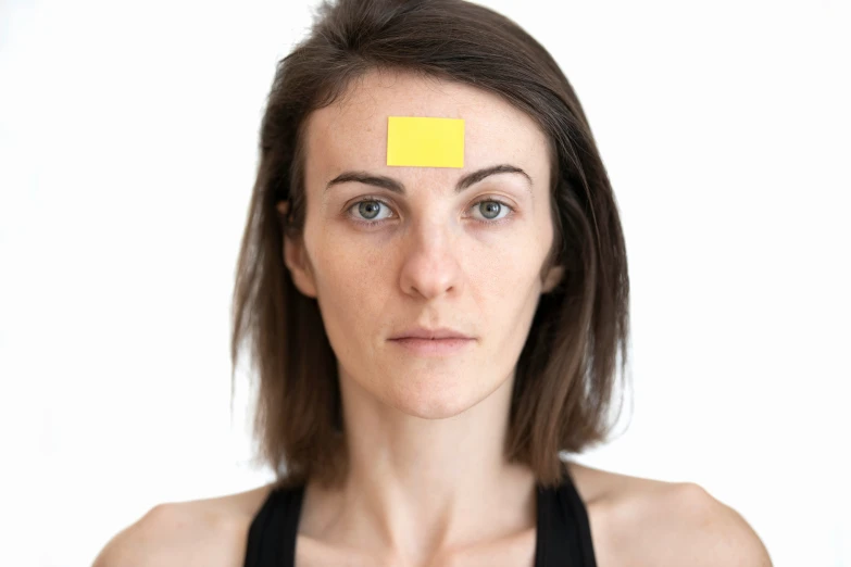 a woman's face with a piece of yellow sticker on the forehead