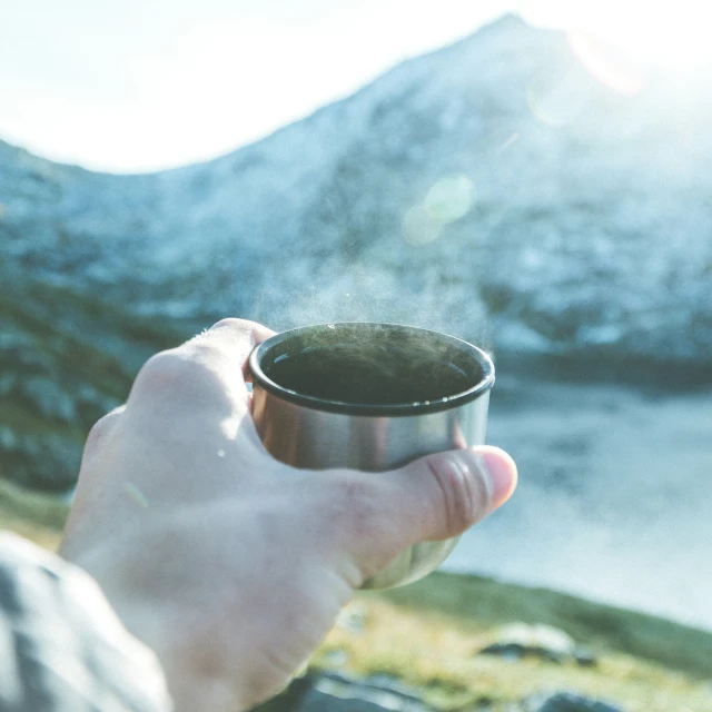 a person holding up a cup with an island in the background