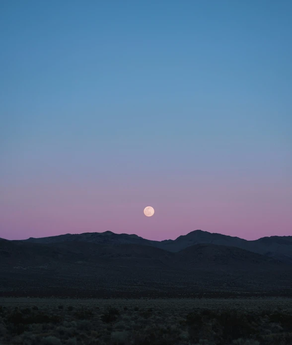 a moon rises behind mountains at dusk