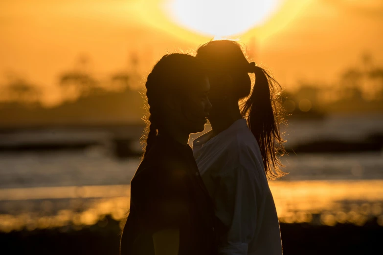 two young women are kissing at sunset over the water