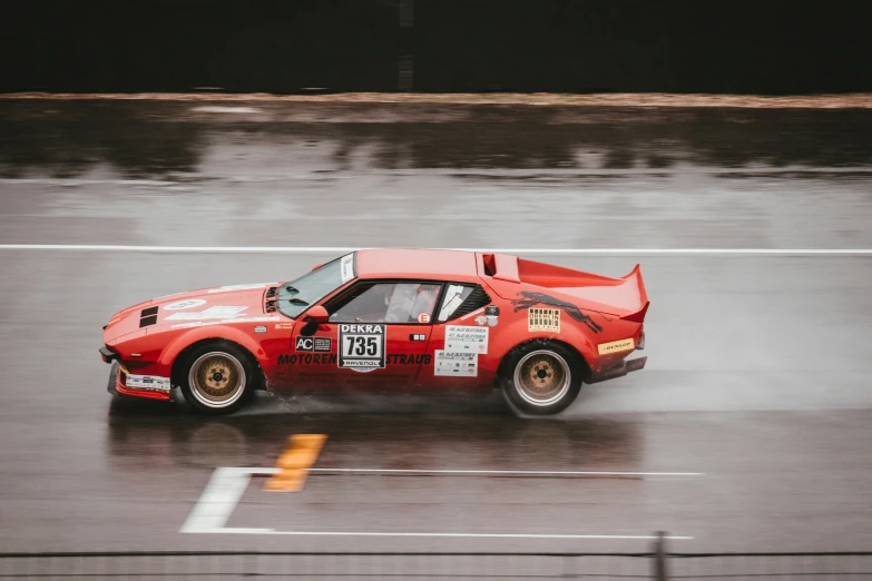 a red car with numbers on it driving through the rain