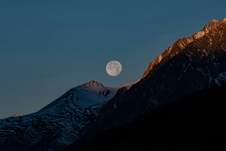 the moon sets over the mountain peak and the snow covered mountains