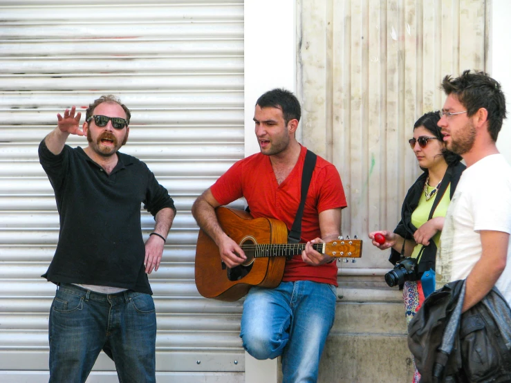 a man is playing a guitar while others stand nearby