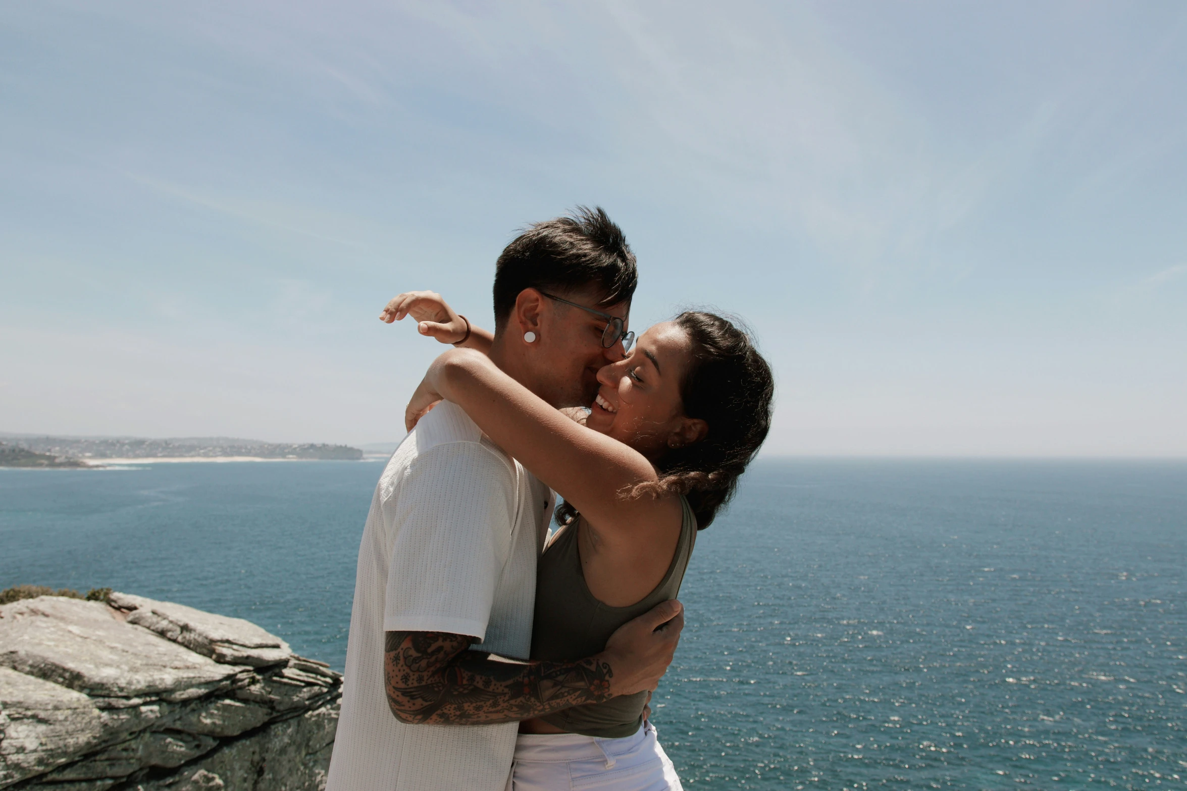 a man and woman hug on a sunny day near the ocean