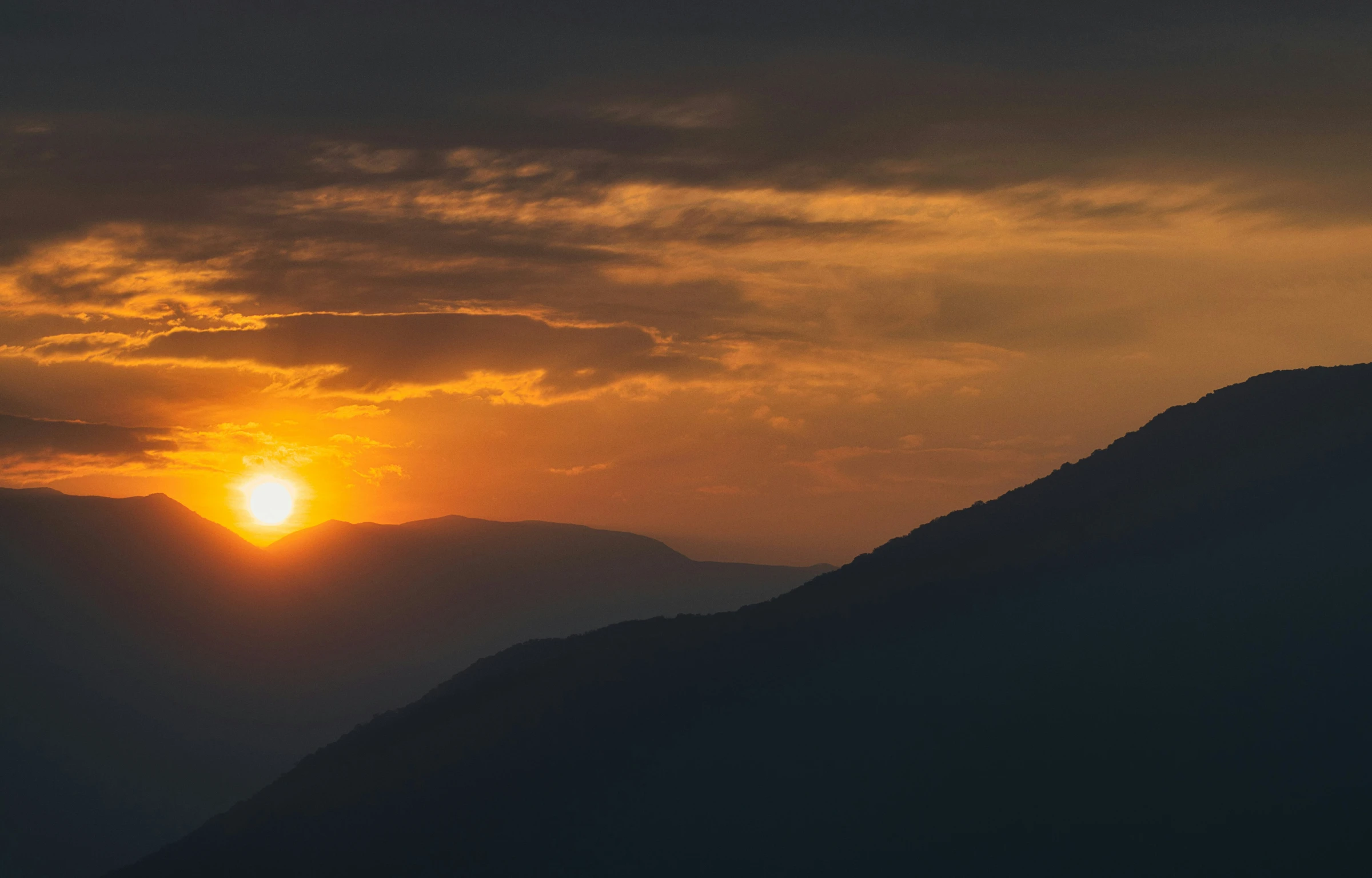 the sun is seen through the dark clouds over mountains