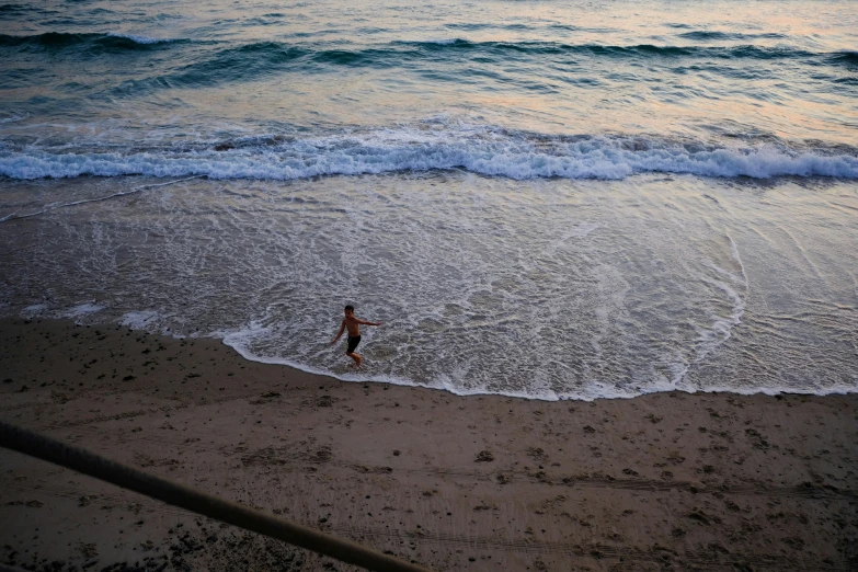 a man walking along the shore line as the sun sets