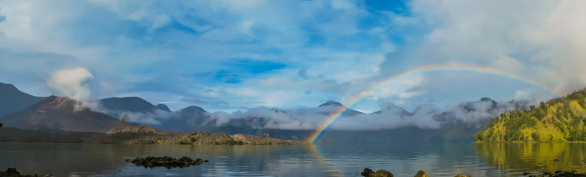 a rainbow in the distance near the water with mountains in the background
