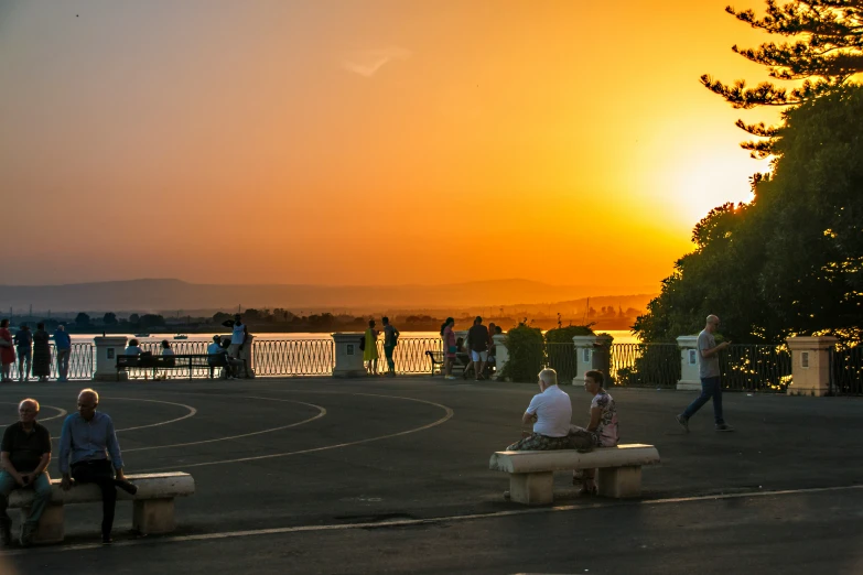 people are sitting around on benches watching the sunset