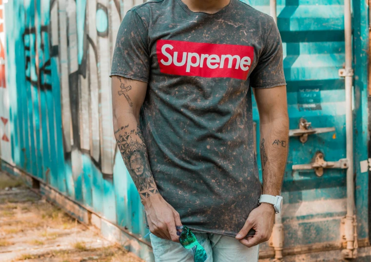 a man wearing a supreme t - shirt standing next to a wall