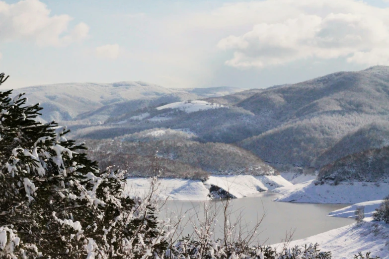 snow covered mountains with some trees and a small lake