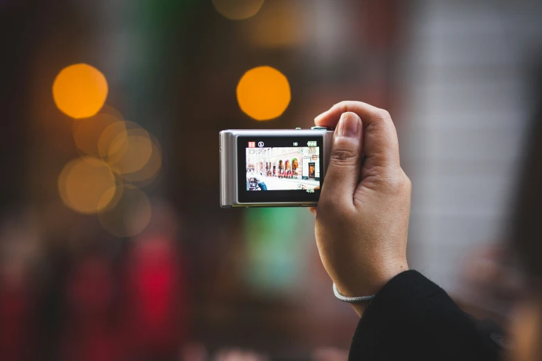 a hand holding a small camera over a street