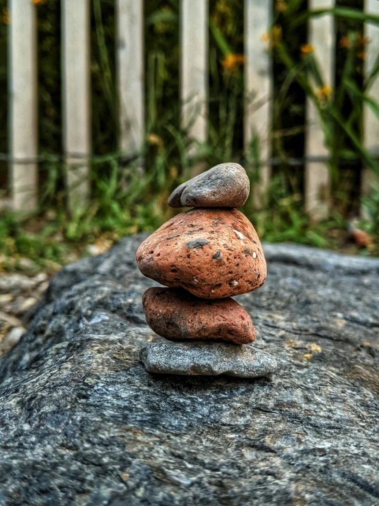 two stacked rocks sitting on a rock by a fence