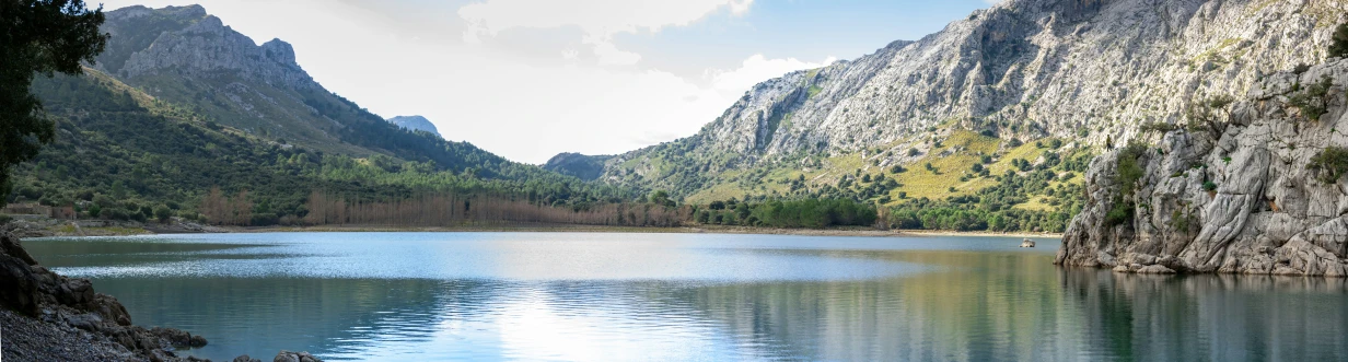 two mountain side cliffs next to a lake with a person riding a bike in the water