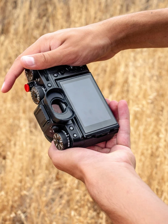 two hands holding an old looking camera outside in a field