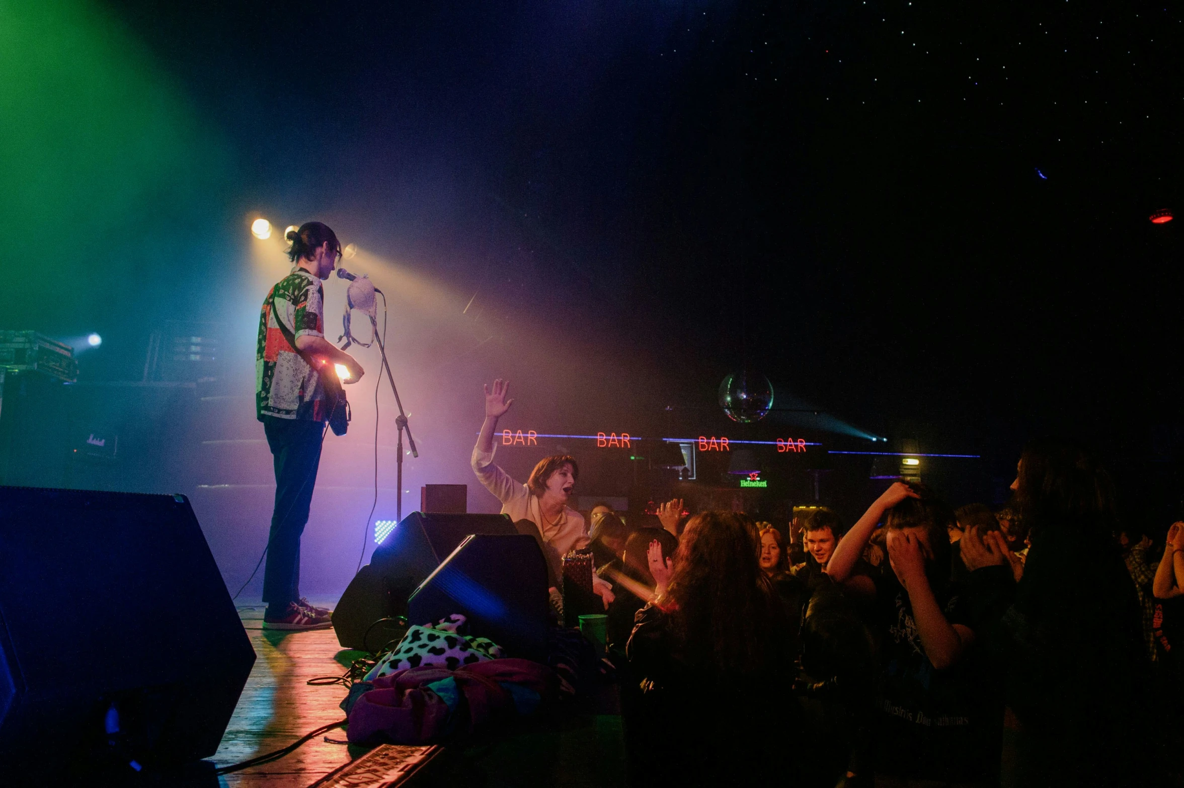 a man on stage with a guitar in his hand while people sit to the side