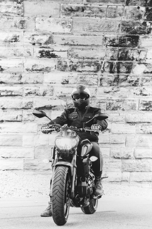 man on a motorcycle sitting on the road next to brick wall