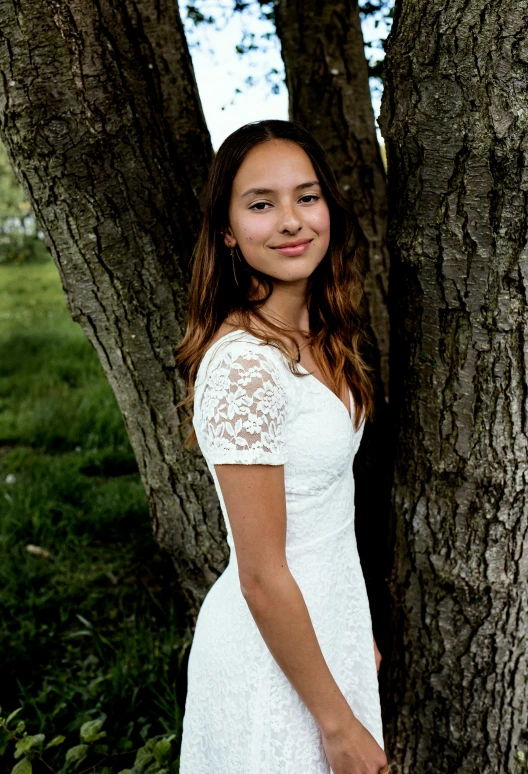 a woman standing next to a tree wearing a white dress