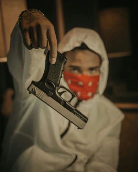 a man in a hood holding a gun and wearing a red bandana