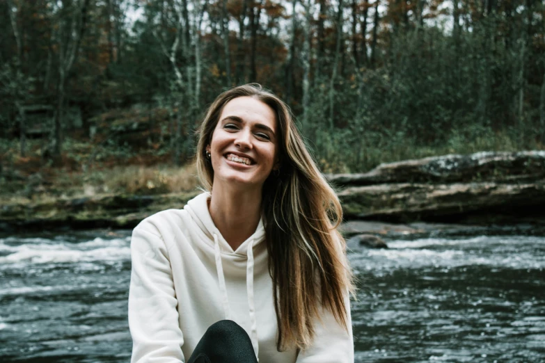 the woman in white sweatshirt is smiling next to the stream