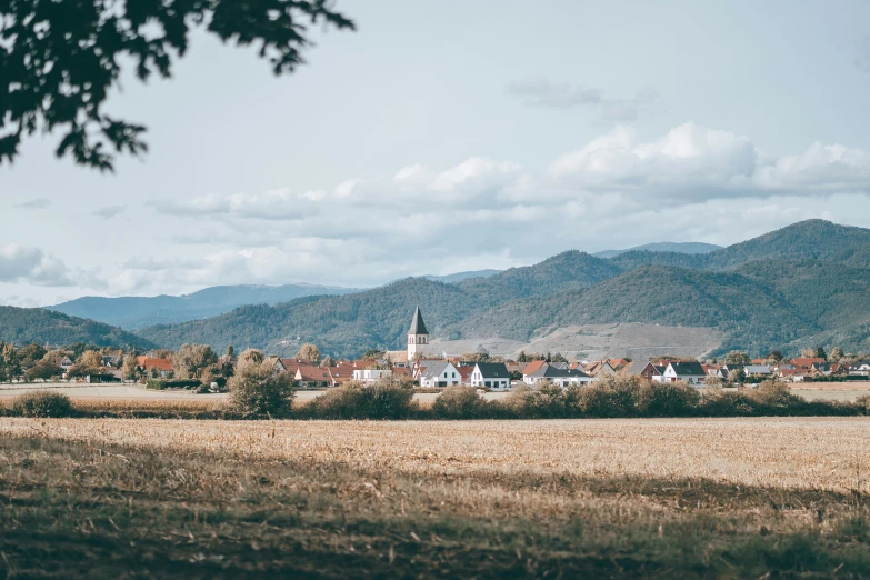 a farm with a church and several mountains behind it