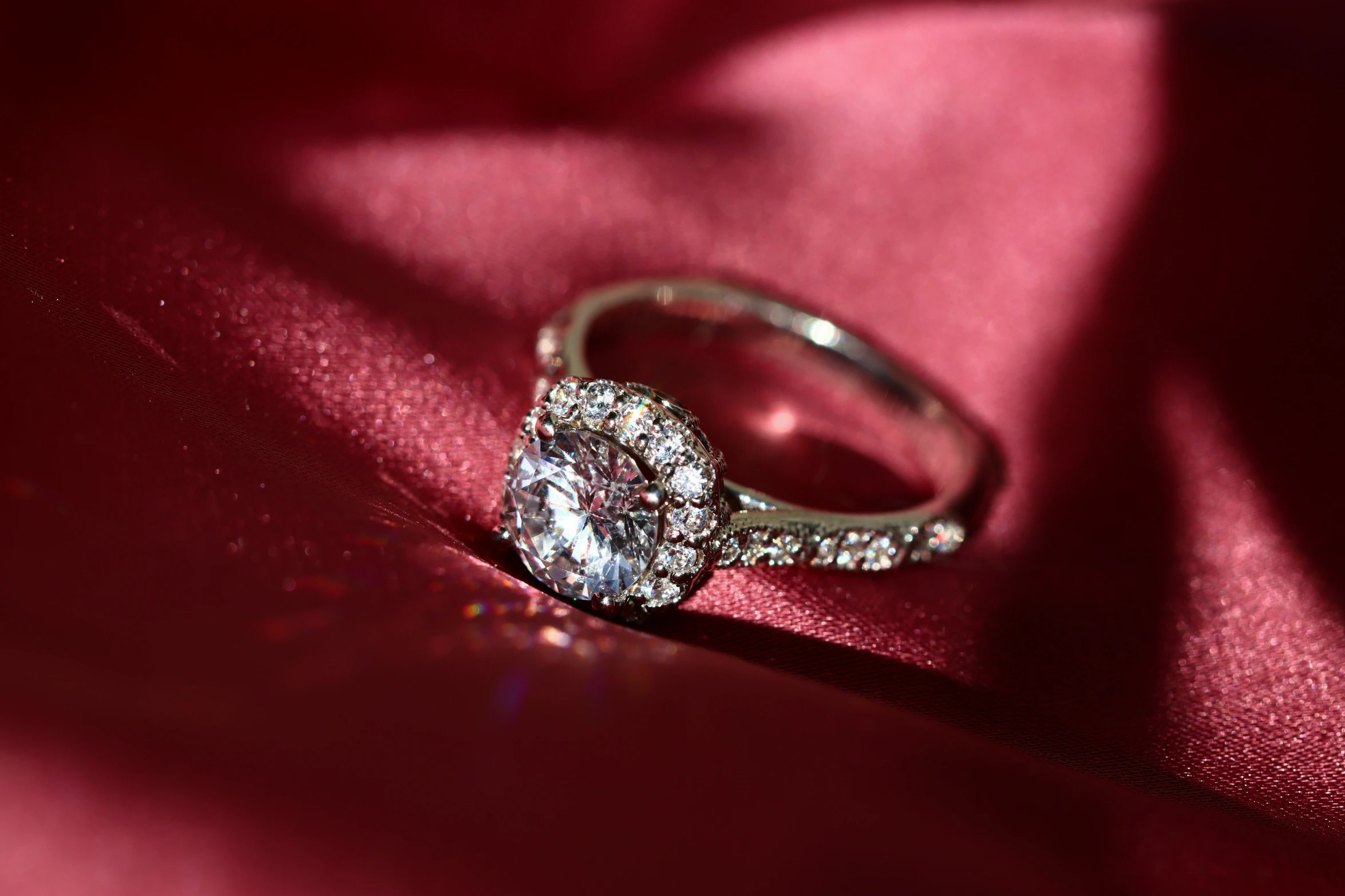 a beautiful round engagement ring sitting on a pink cloth