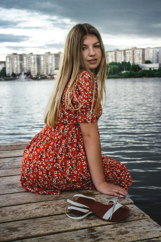 a young woman sitting on a pier wearing an orange dress
