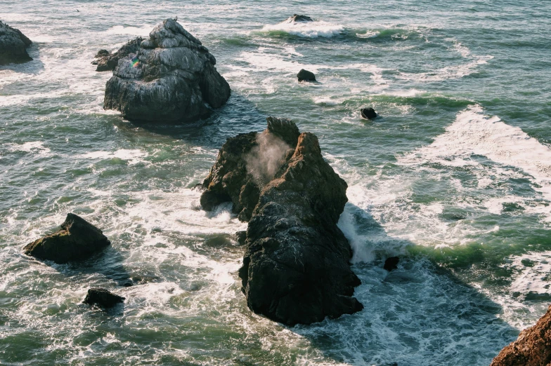 people are in the water on large rocks by the beach