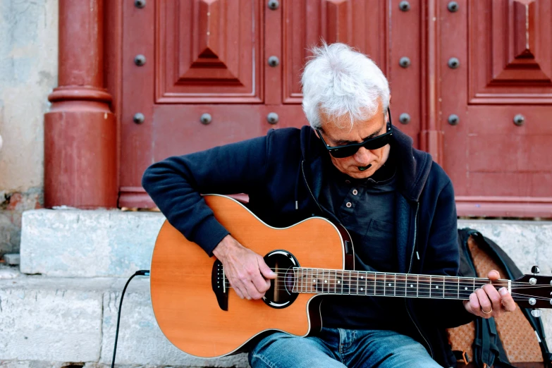 an older man sits on the steps playing his guitar