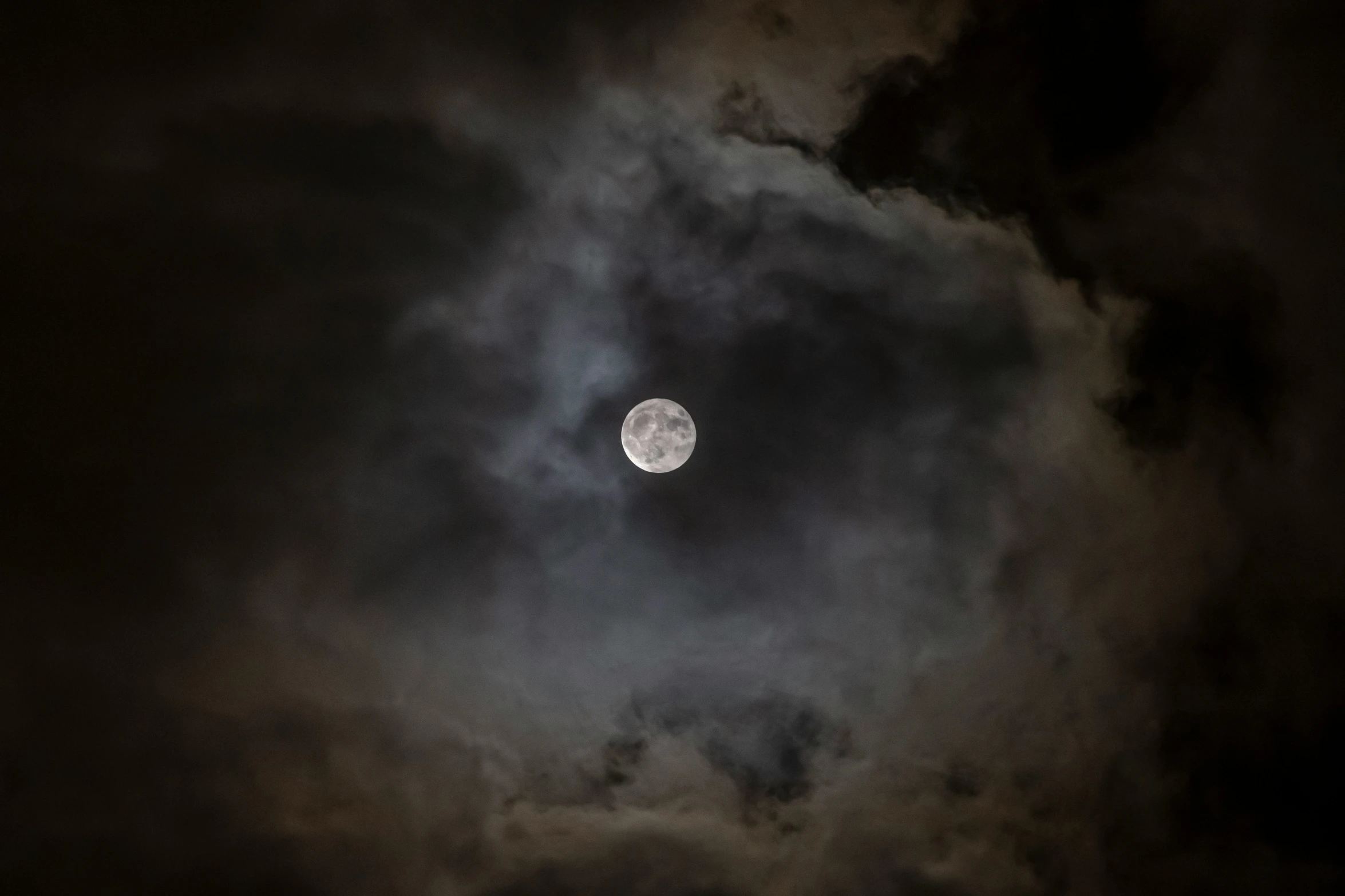 a full moon rising through the dark clouds