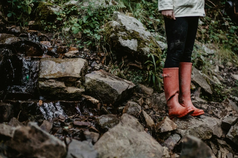 a woman's legs in red rain boots on some rocks