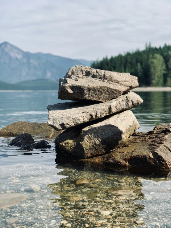 a stack of rocks in the water on a lake shore