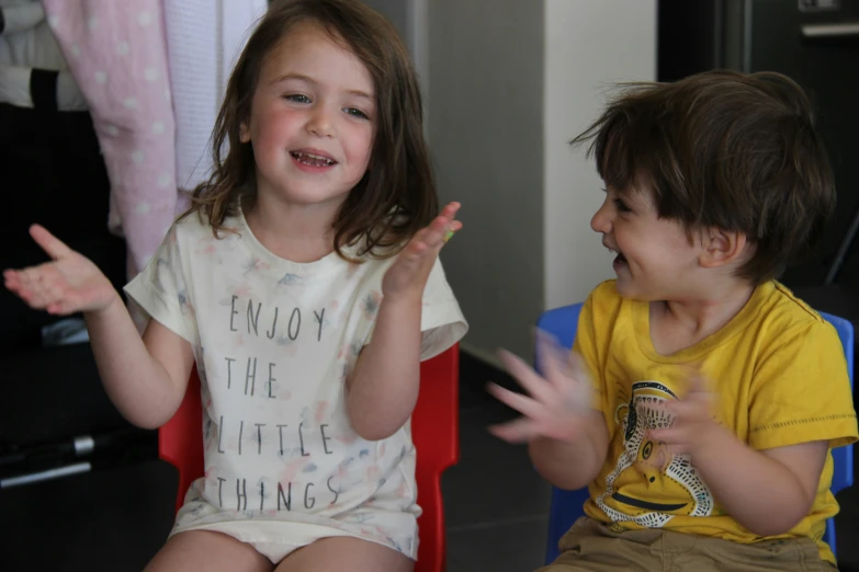 a couple of little s sitting on chairs with their hands in the air