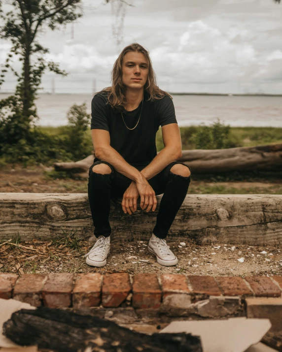 a male in black is posing for a picture by the water