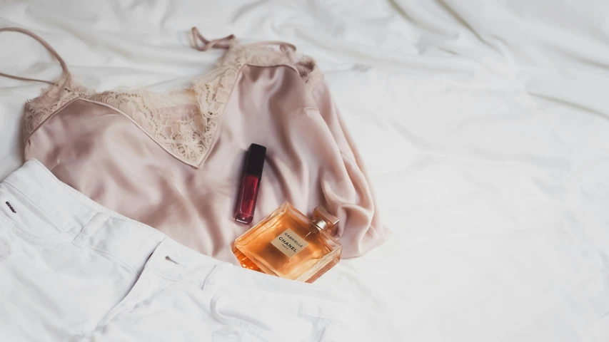 an open top shirt with a lipstick, a bottle of perfume and a pen laying on the bed