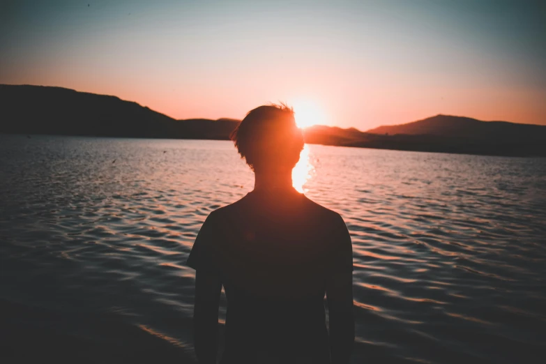 a person stands by the water at sunset